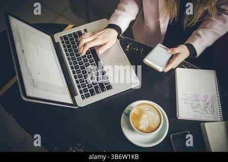 Close-up top view of Caucasian woman's hands Casually dressed student, blogger, writer man working on a laptop holding a phone in his hand, inside the Stock Photo