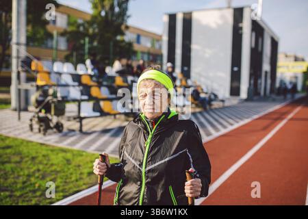 Active rest of the elderly theme. Sports and health in retirement. Caucasian very old woman with deep wrinkles doing Nordic walking exercises with sti Stock Photo