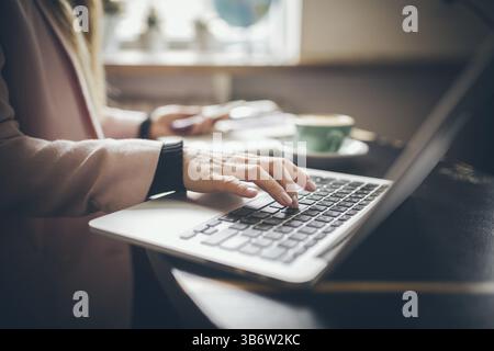 Close-up top view of Caucasian woman's hands Casually dressed student, blogger, writer man working on a laptop holding a phone in his hand, inside the Stock Photo