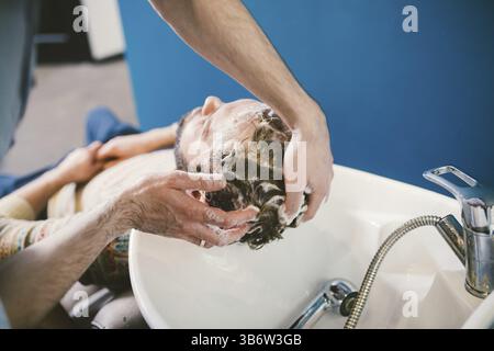 Barbershop theme. Hairdresser for washing hair in a barbershop. Hands male hairdresser close-up washes hair with foam and shampoo Caucasian man with b Stock Photo