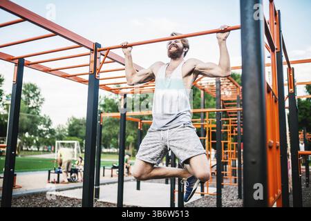 Strong athlete doing pull-up on horizontal bar. Muscular man doing pull ups on horizontal bar in park. Gymnastic Bar During Workout. training strongma Stock Photo
