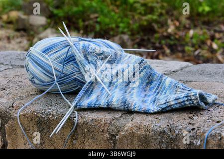 light-blue sock yarn in the process of knitting socks, with knitting needles, lying on a stone surface Stock Photo