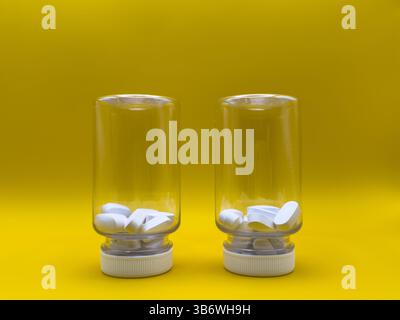 Two transparent inverted jars with white pills inside on yellow background. Front view. Medicine concept. Stock Photo