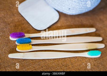 Four bamboo toothbrushes with colorful bristles are arranged on a brown textured surface near a wooden tag Stock Photo