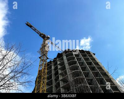 Modern residential building under construction, with cranes and workers. Steel framework rises against clear blue sky, showcasing early stages of urba Stock Photo