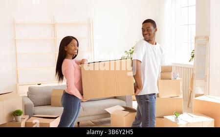 Loving black couple carrying cardboard box together, helping each other in their new home on moving day Stock Photo
