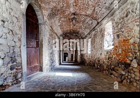 A historic stone corridor with arched ceilings and brick walls, featuring a cobblestone floor and wooden doors. Natural light filters through the wind Stock Photo