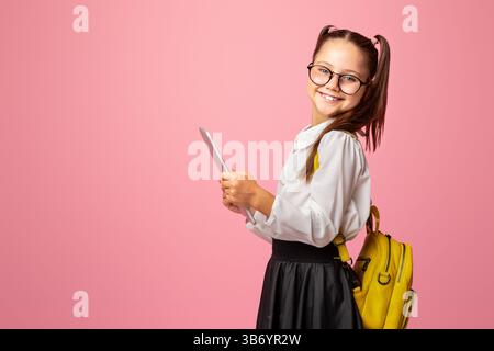 Child using gadgets to study. Cheerful schoolgirl in glasses with backpack holds digital tablet Stock Photo