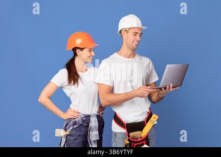 Happy young couple in hardhats using laptop, ordering materials for repair apartment Stock Photo