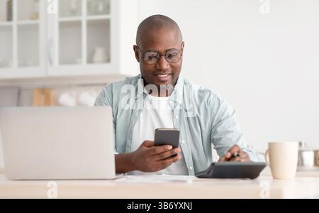 Savings and finances concept. Mature black man using calculator, phone and laptop computer Stock Photo