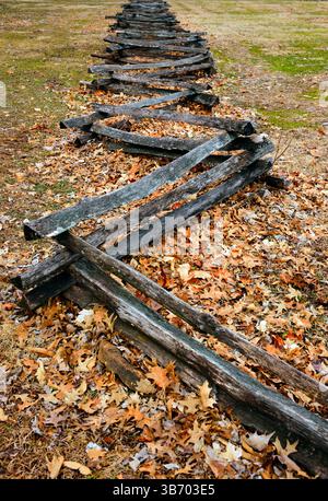 Split rail fence during the fall-winter season with leaves covering the grass. Stock Photo