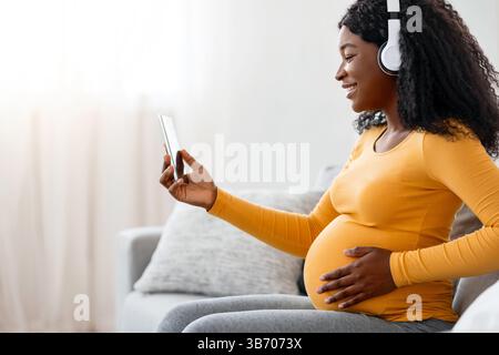 Pregnant black lady enjoying music, using mobile app Stock Photo