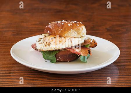 egg bacon and arugula sandwich on a small pretzel bun and white plate Stock Photo