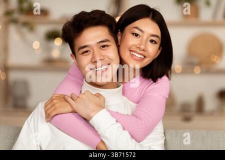 Asian Couple Hugging Smiling Posing Sitting On Sofa At Home Stock Photo