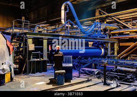 Factory engineer operates pipe painting automatic machine. Stock Photo