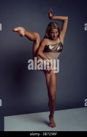 a ballerina in a bodysuit stands on one leg supporting the other leg raised up with one hand Stock Photo