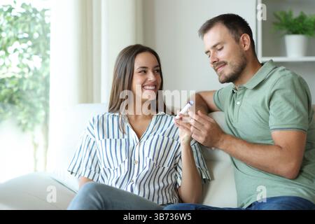 Couple or friends vaping and sharing vaper sitting on a couch at home Stock Photo