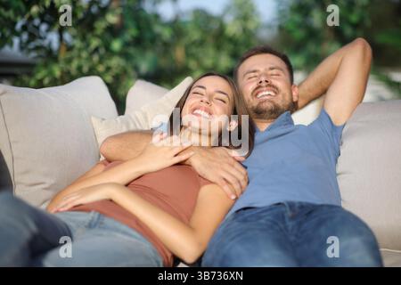 Happy couple enjoying resting in a terrace lying on a couch at home Stock Photo