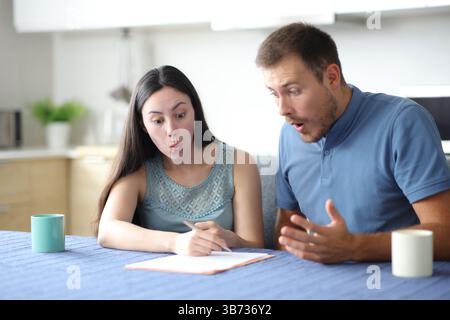 Surprised interracial couple checking contract in the kitchen at home Stock Photo