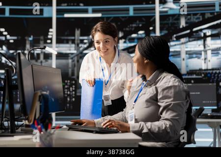 Teamworking colleagues in server hub pleased after successful operations. Happy data center engineering team checking infrastructure health report showing stable performance indicators Stock Photo