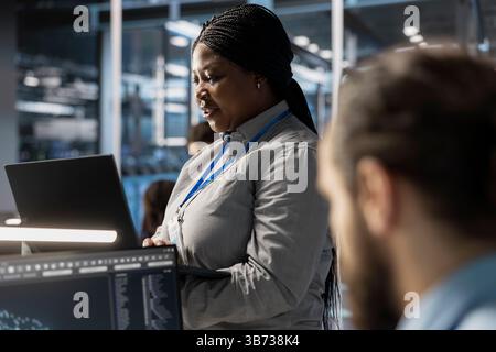 Technician using laptop to oversee server infrastructure powering algorithm training and data inference tasks. Employee using notebook to do maintenance on supercomputers supporting analytics workload Stock Photo