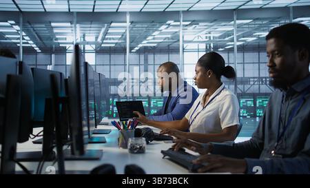 Technicians using computers and tablet in data center, implementing AI systems. Server farm experts using artificial intelligence on device to identify hardware failures impacting operations, camera A Stock Photo
