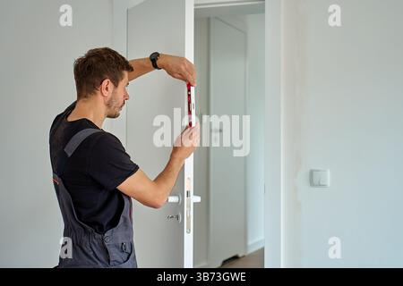 Worker checking vertical alignment of door with bubble level. Professional installing interior door. Home renovation Stock Photo