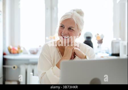 Mature woman working with her laptop at home kitchen Stock Photo