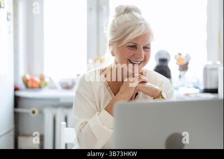 Mature woman working with her laptop at home kitchen Stock Photo