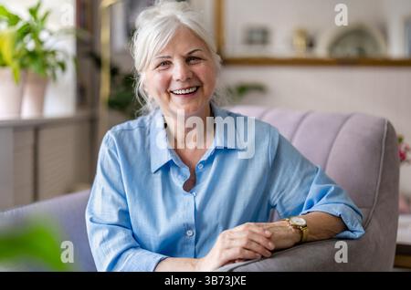 Happy senior woman at home sitting in armchair and looking at camera Stock Photo