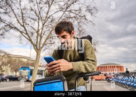 Young delivery man riding a bicycle through the city, using a smartphone app for navigation and managing online orders efficiently Stock Photo