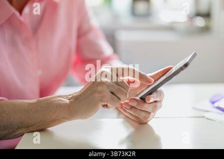 Close-up of an elderly woman's hands using a mobile phone at the kitchen table Stock Photo