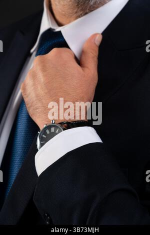 Close-up of a mature man in suit adjusting his shirt collar, revealing a luxury wristwatch, emphasizing style, confidence, and professionalism. Stock Photo