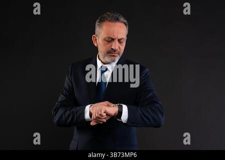 Mature businessman in suit looking at his wristwatch, symbolizing time management, punctuality or urgency. Stock Photo