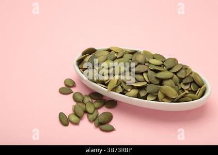 Pumpkin seeds in white plate on pink background. Top view Stock Photo
