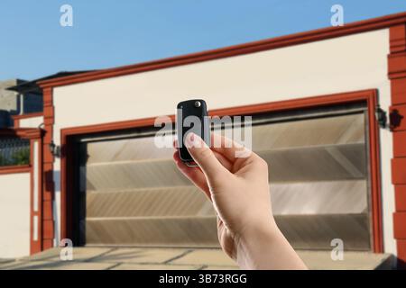Woman using remote to control garage door outdoors, closeup Stock Photo