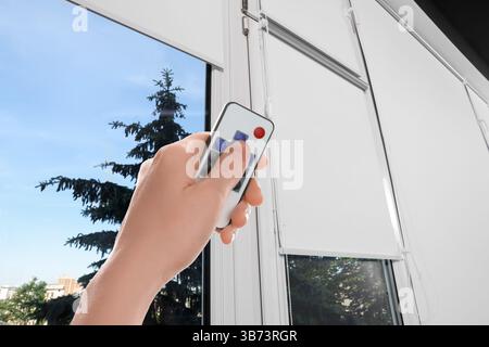 Woman using remote to control blinds in room, closeup Stock Photo