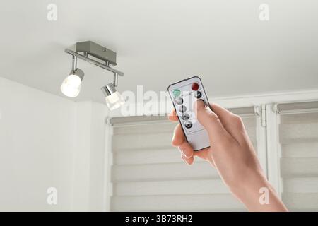 Woman using remote to control lighting in room, closeup Stock Photo