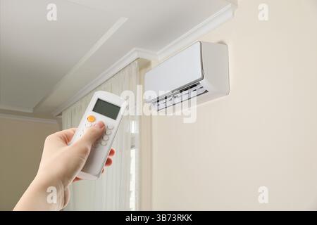 Woman using remote to control air conditioner in room, closeup Stock Photo