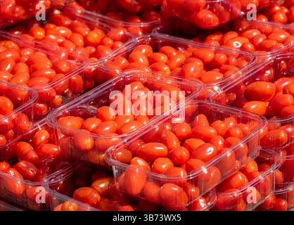 Fresh, vibrant red cherry tomatoes packed in clear plastic containers, stacked neatly for sale at a market. Stock Photo