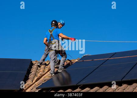 Two technicians working on photovoltaic plant on rooftop securing solar panel on sunny day Stock Photo