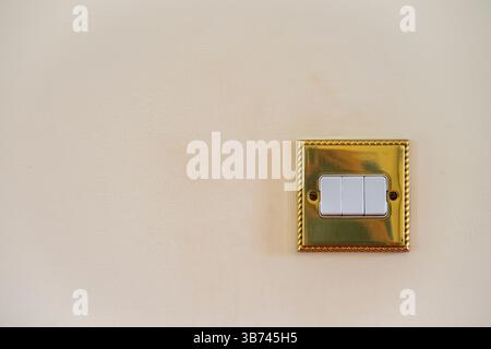 Triple light switch. Gold switch with white details and magnolia wall. All switches in off position. No branding. Copy space to left. Stock Photo
