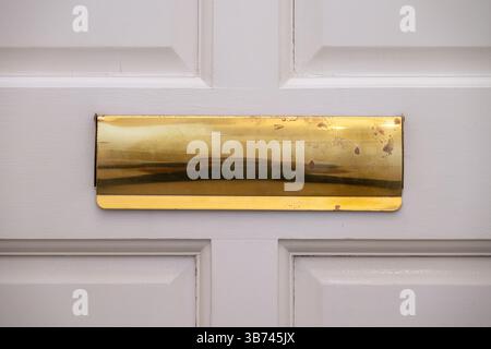Close up of a gold-colored letter box on a white door. Old and worn. Stock Photo