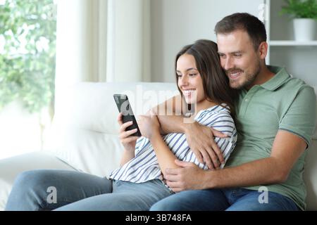 Happy couple using mobile phone together sitting ona couch at home Stock Photo
