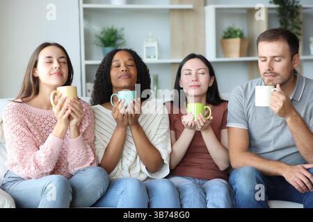 Group of four friends smelling drinks sitting on a couch at home Stock Photo