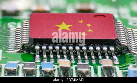 A close-up view of a microchip featuring the Chinese flag printed on its surface, surrounded by electronic components on a green circuit board, reflec Stock Photo
