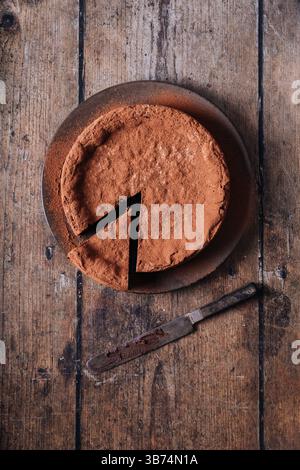 A cocoa dusted rustic chocolate cake on a brown plate with a single piece cut out Stock Photo