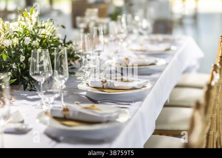 A wedding table covered with a white tablecloth, decorated with flowers, candles, glasses and cutlery. Stock Photo