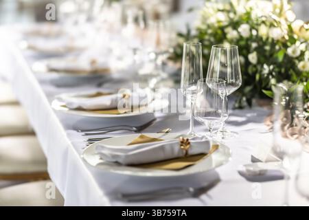 A wedding table covered with a white tablecloth, decorated with flowers, candles, glasses and cutlery. Stock Photo