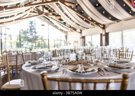 Wedding setting and decorated tables in a beautiful modern interior of a performance hall with a modern light ceiling of wooden construction. Stock Photo